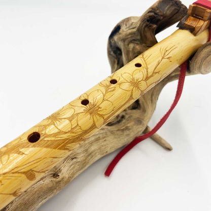 Flûte amérindienne en bambou gravée de fleurs de cerisier, avec totem en bois d’olivier et lacet rouge, accordée en La 432Hz.
