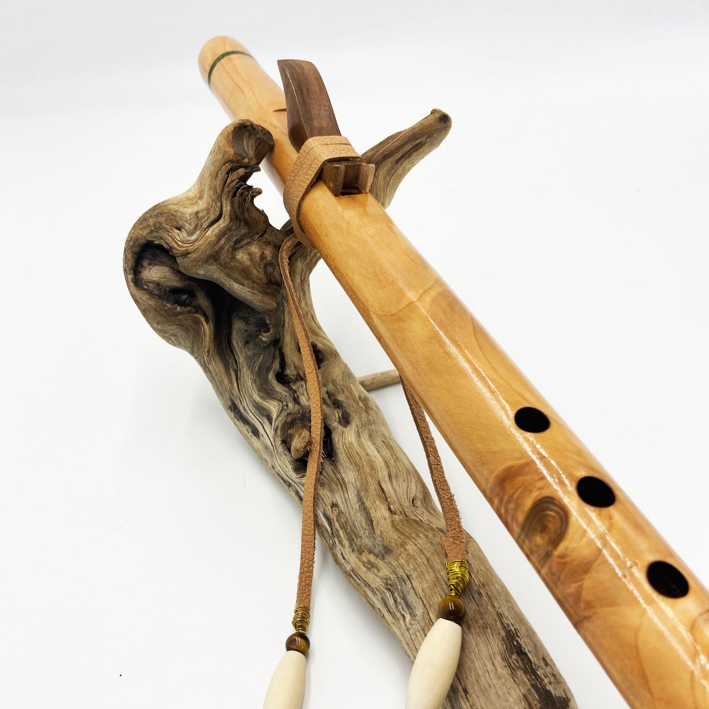 Flûte amérindienne artisanale en bois de cèdre clair, totem en noyer, ornements plumes violettes et turquoises, posée sur un support en bois flotté naturel.