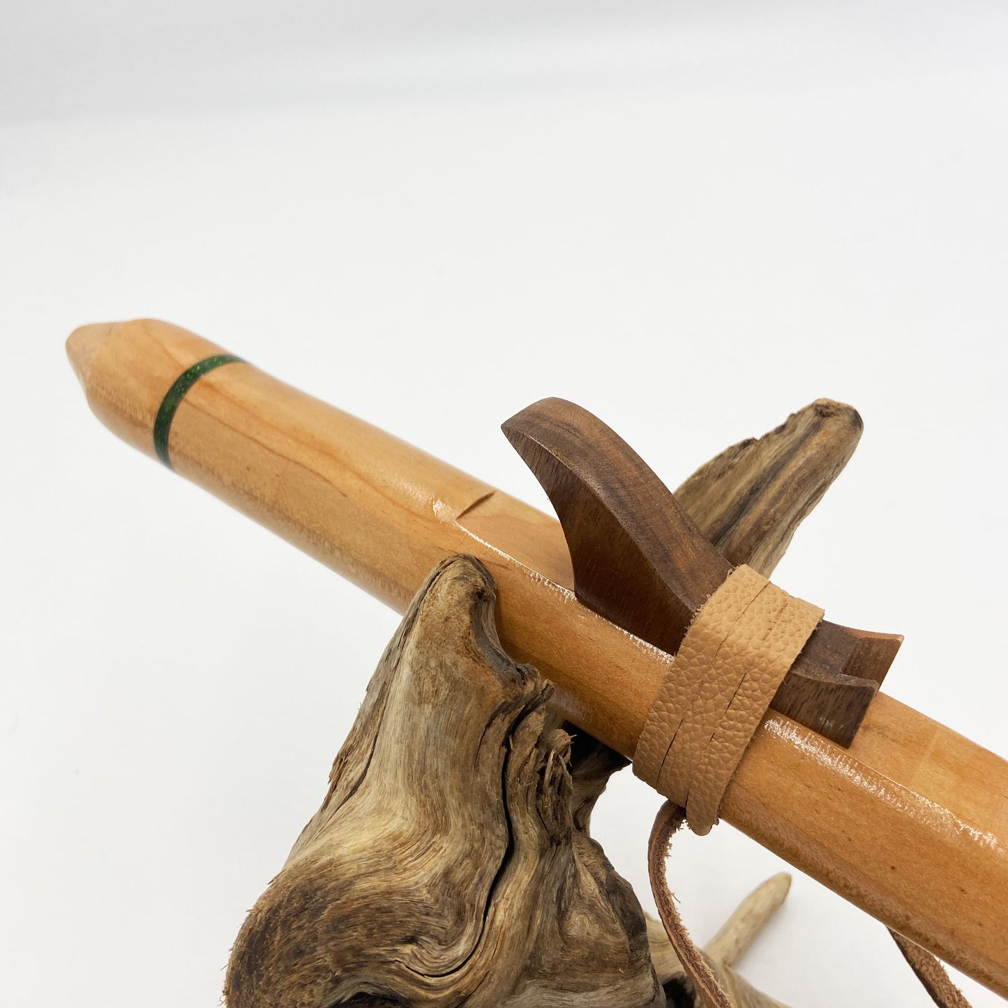 Flûte amérindienne artisanale en bois de cèdre clair, totem en noyer, ornements plumes violettes et turquoises, posée sur un support en bois flotté naturel.