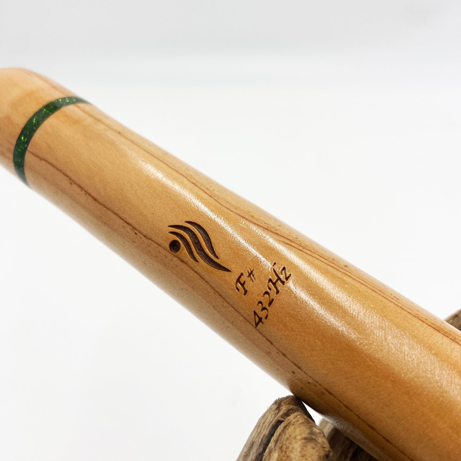 Flûte amérindienne artisanale en bois de cèdre clair, totem en noyer, ornements plumes violettes et turquoises, posée sur un support en bois flotté naturel.