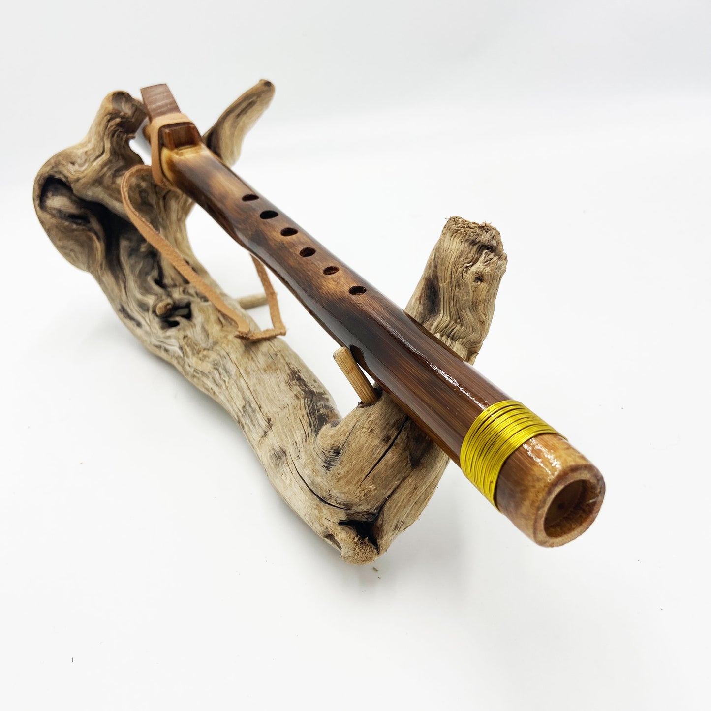 Flûte amérindienne en bambou effet caramel et noirci, embouchure en bois d'olivier veiné, totem en noyer et lacet de cuir sur support en bois flotté. Détail de fil doré à la base.