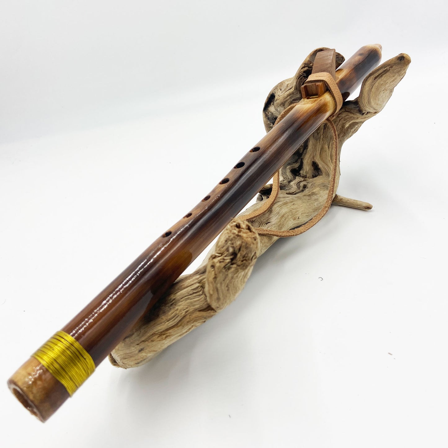 Flûte amérindienne en bambou effet caramel et noirci, embouchure en bois d'olivier veiné, totem en noyer et lacet de cuir sur support en bois flotté. Détail de fil doré à la base.