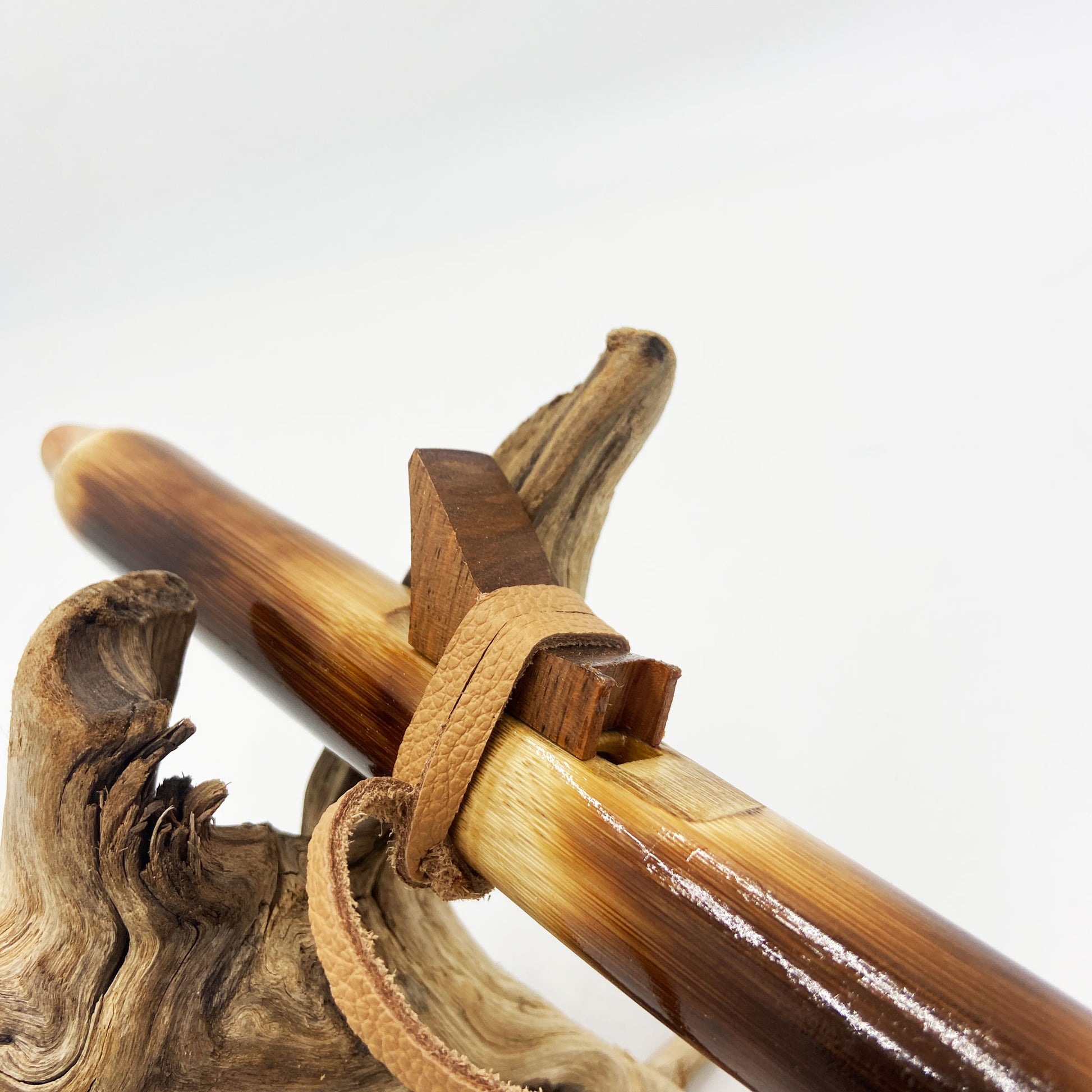 Flûte amérindienne en bambou effet caramel et noirci, embouchure en bois d'olivier veiné, totem en noyer et lacet de cuir sur support en bois flotté. Détail de fil doré à la base.