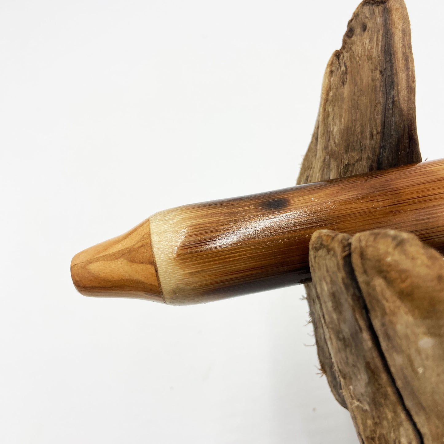 Flûte amérindienne en bambou effet caramel et noirci, embouchure en bois d'olivier veiné, totem en noyer et lacet de cuir sur support en bois flotté. Détail de fil doré à la base.