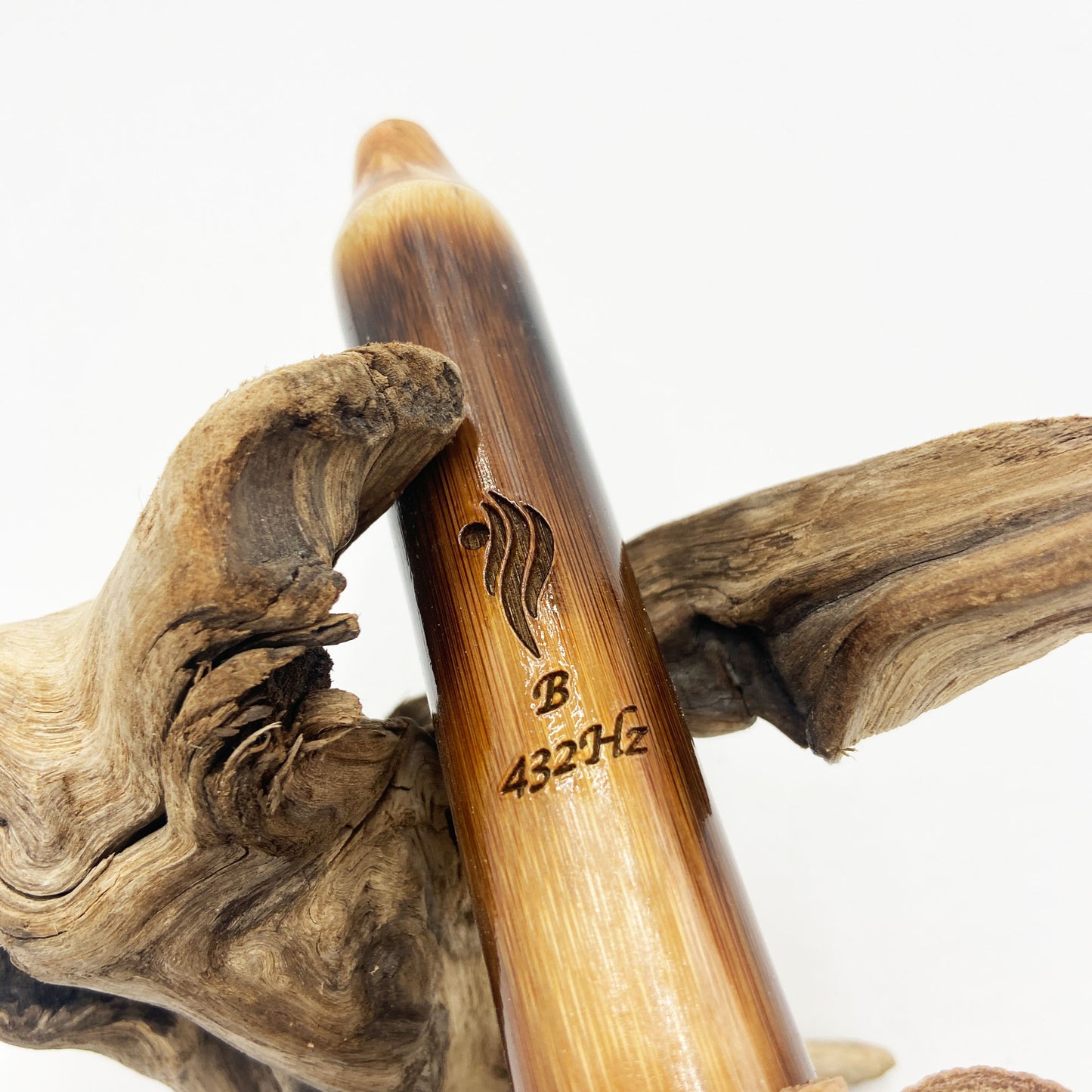 Flûte amérindienne en bambou effet caramel et noirci, embouchure en bois d'olivier veiné, totem en noyer et lacet de cuir sur support en bois flotté. Détail de fil doré à la base.