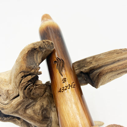 Flûte amérindienne en bambou effet caramel et noirci, embouchure en bois d'olivier veiné, totem en noyer et lacet de cuir sur support en bois flotté. Détail de fil doré à la base.