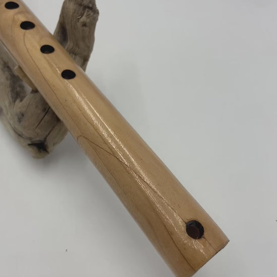 Flûte amérindienne artisanale en bois de cèdre clair, totem en noyer, ornements plumes violettes et turquoises, posée sur un support en bois flotté naturel.