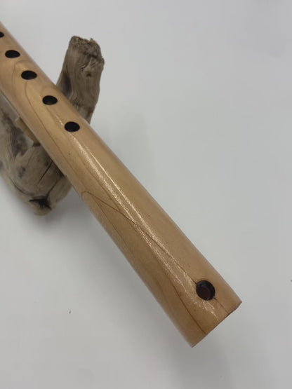 Flûte amérindienne artisanale en bois de cèdre clair, totem en noyer, ornements plumes violettes et turquoises, posée sur un support en bois flotté naturel.